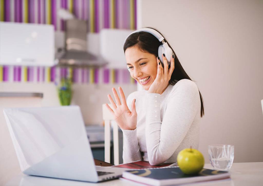 Girl in pink headphones talking to someone on laptop
