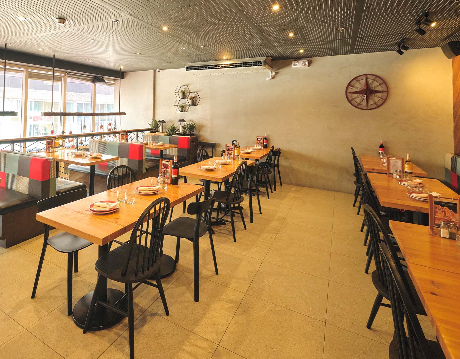 Rustic, Industrial Vibe—Evoking a cozy ambiance, the main dining hall is lined with wooden tables and black chairs. The cluster of hanging lanterns, and the bold red panel by the staircase dotted with various chopping boards lend whimsy, while the exposed beams make the place a modern yet functional space.