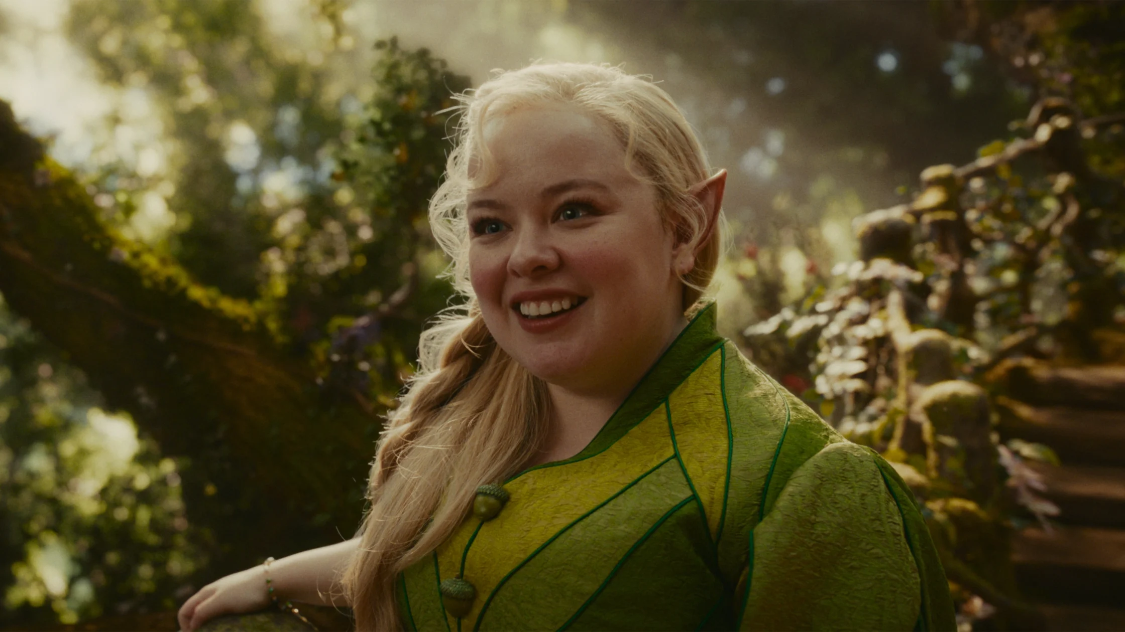 Smiling woman in a lime-green fantasy costume with pointy elf ears outdoors in a sunlit garden park.