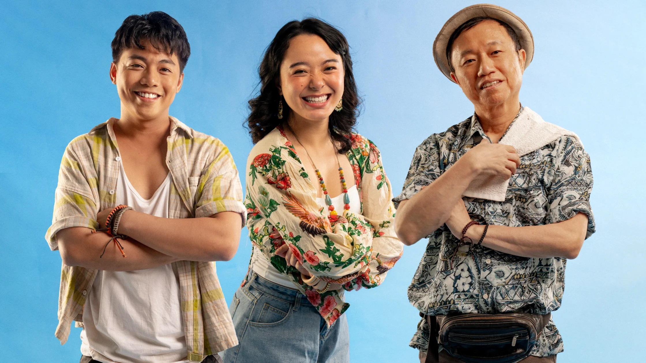 Three friends posing with crossed arms and big smiles against a blue backdrop.