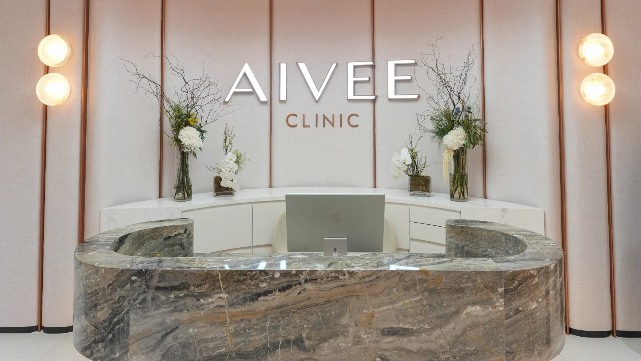 Reception desk at AIVEE CLINIC with a curved marble counter and flower arrangements, laptop on the desk
