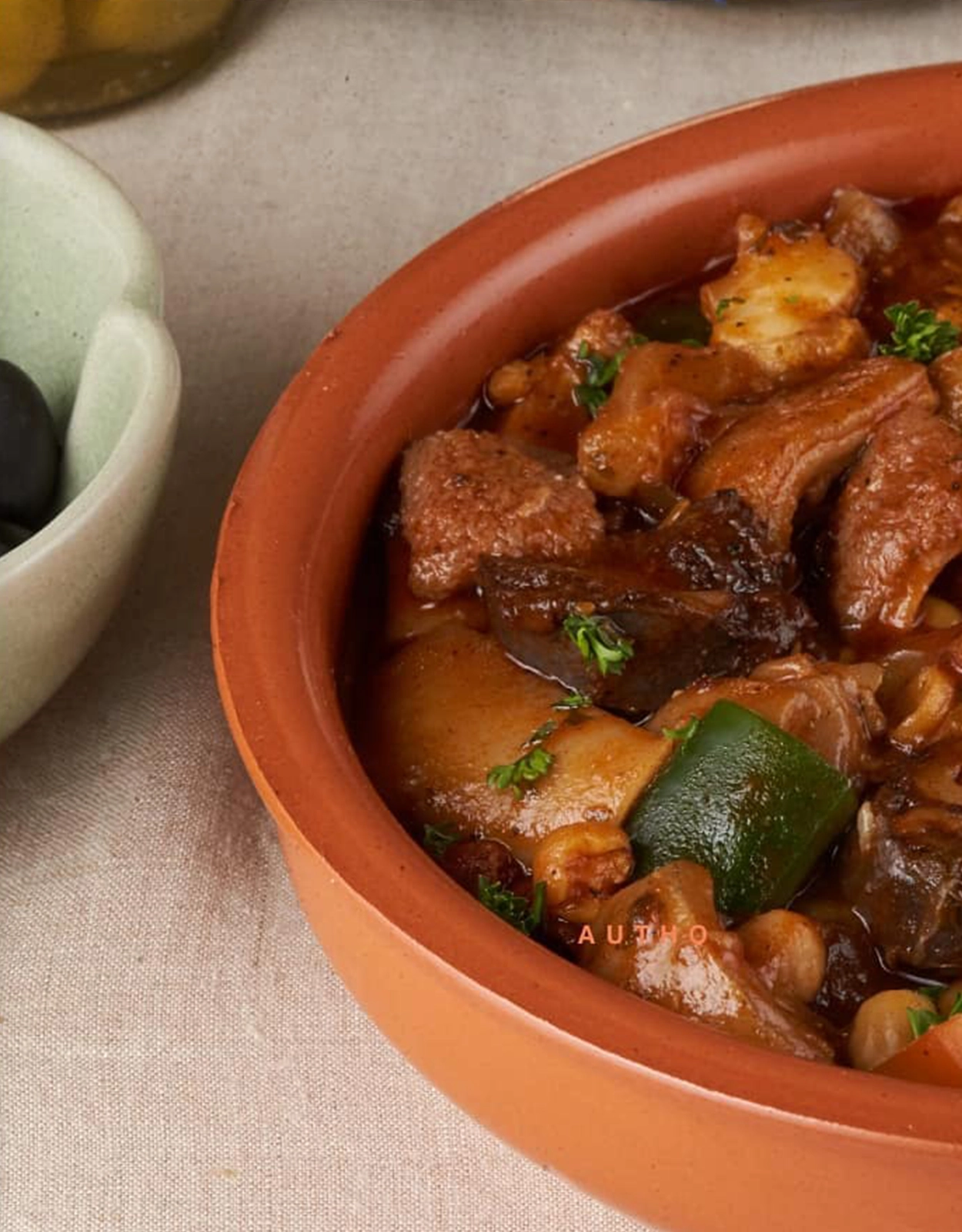 Beef stew with chunks of meat and vegetables in a tomato-based sauce served in a terracotta pot, garnished with herbs
