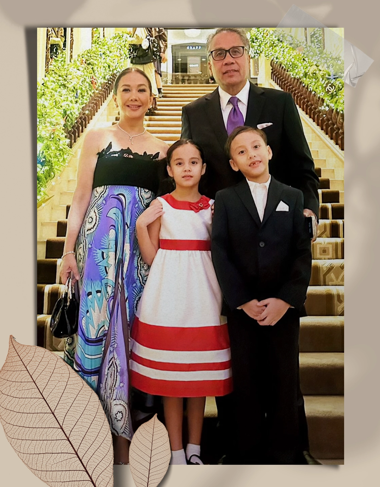 Family of four posing on a grand staircase: mother in a colorful strapless dress, father in a black suit with purple tie, daughter in a white dress with red stripes, son in a black suit.