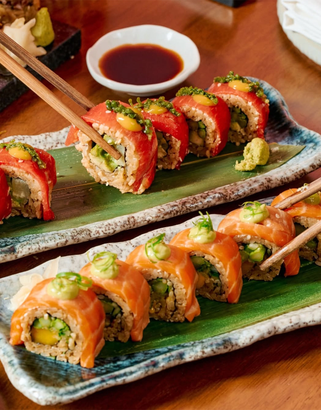 Assorted sushi rolls topped with salmon, avocado and cucumber on a ceramic platter with wasabi nearby.