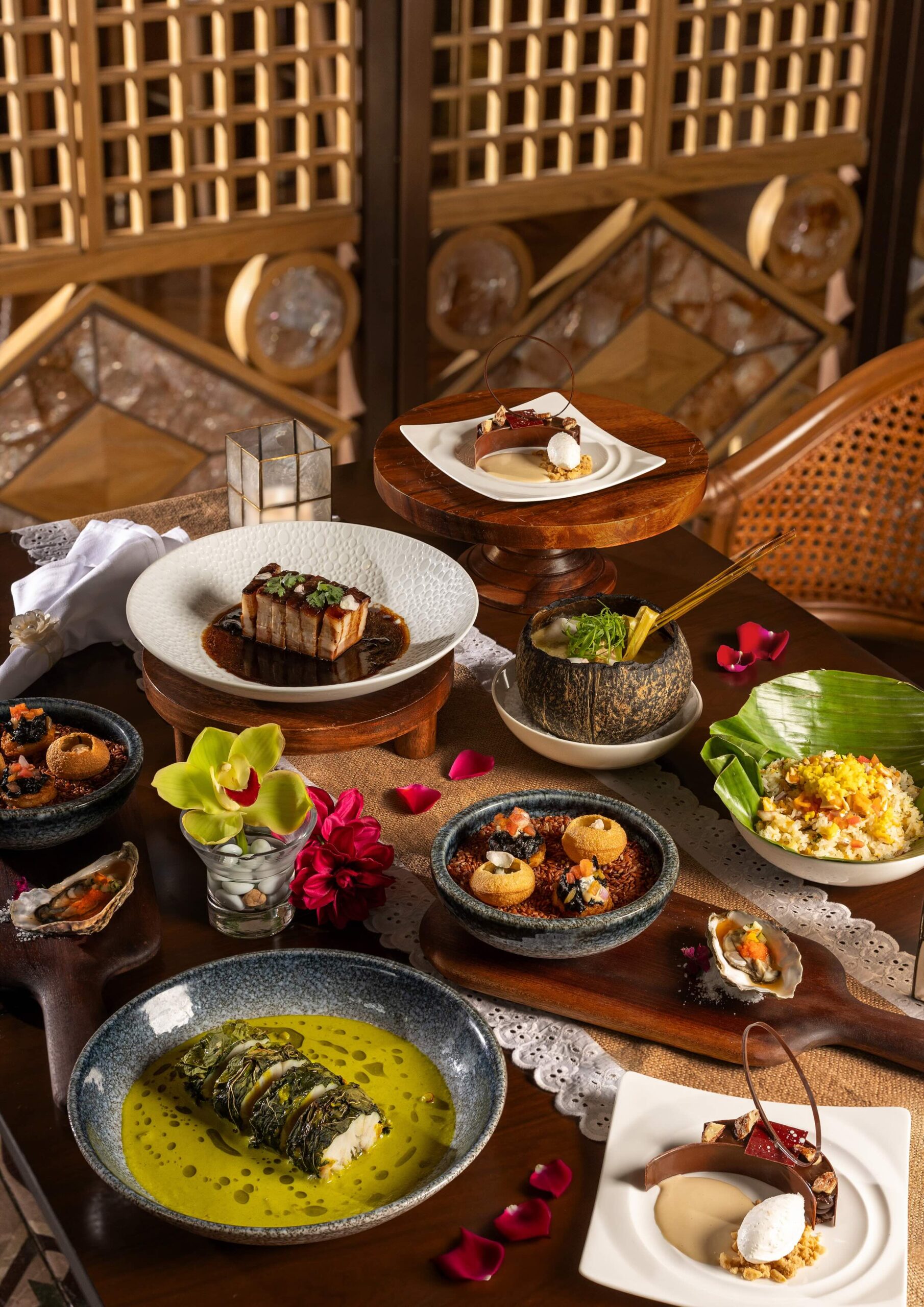 A lavish Asian-inspired feast on a wooden table with colorful dishes, desserts, and flowers.